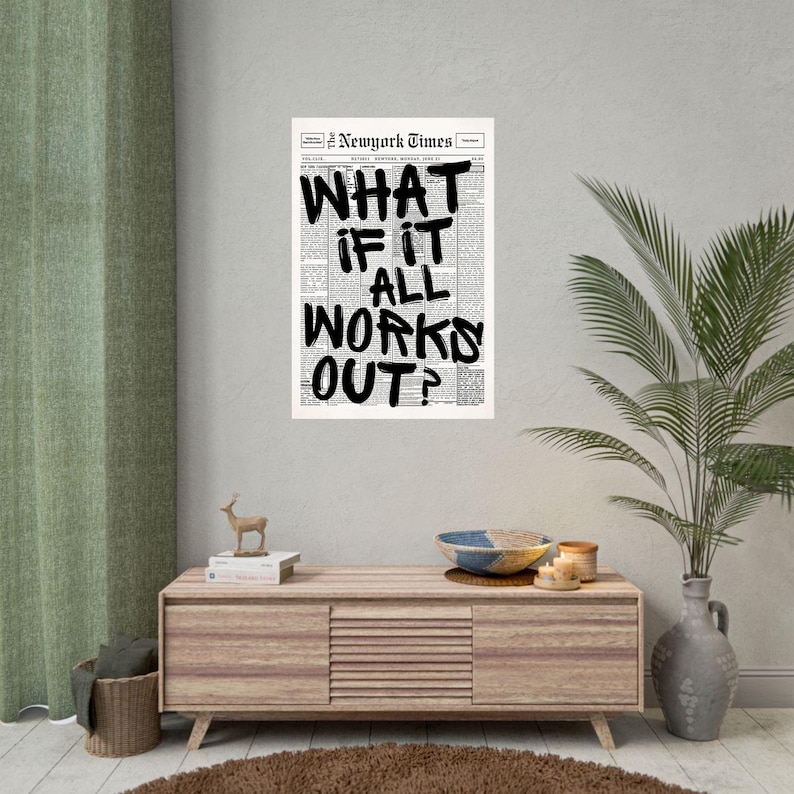 May include: A black and white print of a newspaper page with the headline "WHAT IF IT ALL WORKS OUT?" in bold, handwritten-style lettering. The print is displayed on a wall above a wooden cabinet with decorative items.