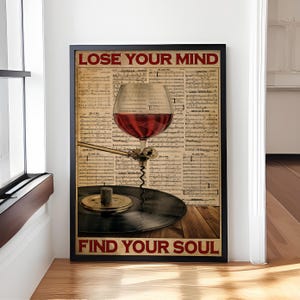 May include: A vintage-style poster with the text "Lose Your Mind Find Your Soul" in red and black lettering. A glass of red wine is placed on a record player turntable, with a corkscrew attached to the tonearm. The background is a sheet of music.