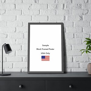 以下が含まれることがあります： 「Sample Black Framed Poster USA Only」のテキストと小さなアメリカ国旗が入った黒いフレームのポスター。 ポスターは、白いレンガの壁を背景に、黒い表面に表示されています。