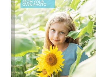 May include: A rectangular canvas print featuring a photograph of a child with long blonde hair wearing a light blue shirt, standing in a field of bright yellow sunflowers. The top left corner displays a light blue box with the white text CUSTOM CANVAS FROM YOUR OWN PHOTO.