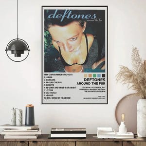 May include: A framed poster featuring the album art for Deftones' "Around the Fur." The image shows a person in a black top, with the band's name and album title at the top. The tracklist and release information are also visible.