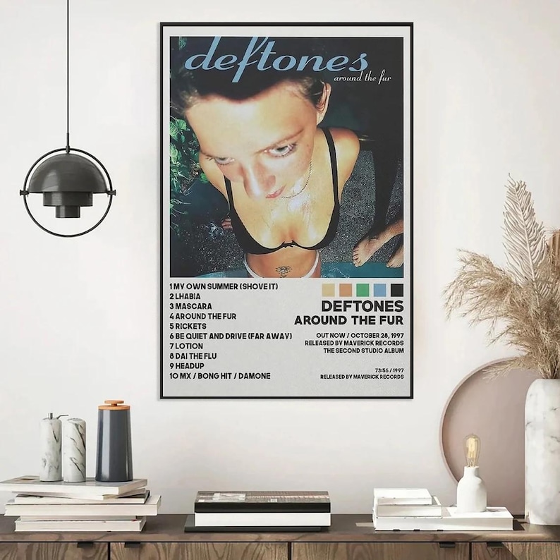 May include: A framed poster featuring the album art for Deftones' "Around the Fur." The image shows a person in a black top, with the band's name and album title at the top. The tracklist and release information are also visible.