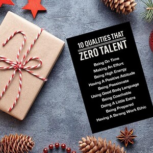 May include: A festive holiday scene with a wrapped gift, pine cones, and ornaments. The gift is wrapped in brown paper and tied with red and white twine. A black card lists "10 Qualities That Zero Talent" in white text.
