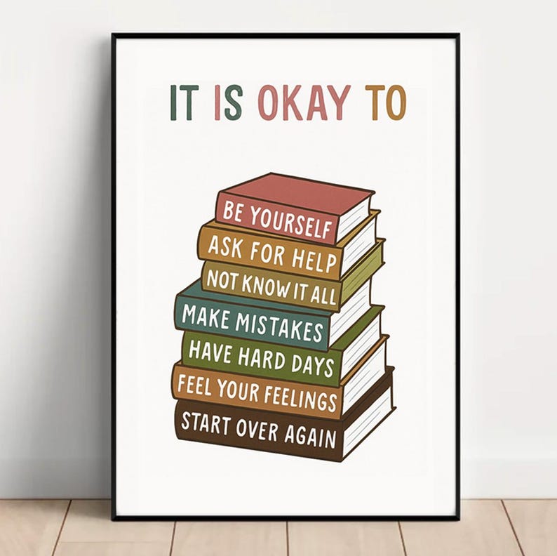 May include: A framed print with the text "IT IS OKAY TO" above a stack of books. Each book has a different title, including "BE YOURSELF" and "START OVER AGAIN". The color palette includes shades of brown, green, and pink.
