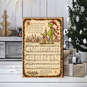 May include: A rectangular print featuring a green character wearing a red and white hat and scarf, standing next to a dog. The print includes musical notation for a Christmas carol, text about Christmas, and a decorative border of holly leaves.