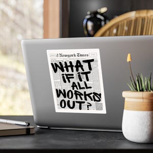 May include: A sticker on a laptop featuring a newspaper-style design with the text "WHAT IF IT ALL WORKS OUT?" in bold, black lettering. The sticker is white with a black and white newspaper background.