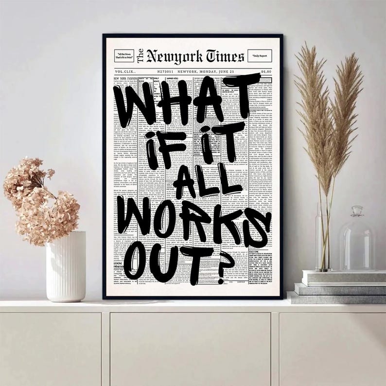 May include: A framed print featuring a newspaper page with the headline "The Newyork Times." Bold black text reads "WHAT IF IT ALL WORKS OUT?" The print is displayed on a white cabinet, with decorative flowers and a vase.