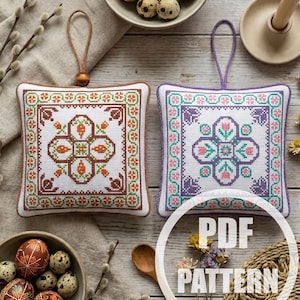 Op de afbeelding: Twee vierkante kruissteekornamenten met bloemmotieven, één bruin en één paars, worden getoond met versierde paaseieren en kwarteleieren. De ornamenten hebben een lus om op te hangen. De afbeelding bevat de tekst "PDF PATTERN".