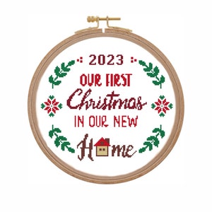 Könnte beinhalten: Ein weißer Stickrahmen mit einem roten und grünen Kreuzstich-Design. Das Design lautet "2023 Unser erstes Weihnachten in unserem neuen Zuhause" mit einem kleinen Haussymbol.