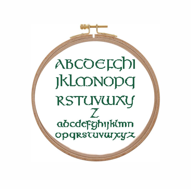 May include: A wooden embroidery hoop with the alphabet in green lettering. The letters are in a traditional font. The letters are in two rows, with the uppercase letters on top and the lowercase letters on the bottom.