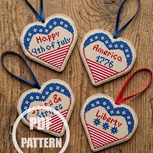 May include: Four heart-shaped ornaments with patriotic themes. Each ornament features a blue and white star-studded border, a red and white striped lower section, and a blue or red ribbon. The ornaments display text such as "Happy 4th of July" and "America 1776".