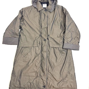 Może przedstawiać: Długi, oliwkowozielony płaszcz z kapturem, zapinany na guziki i z kieszeniami. Kaptur i mankiety rękawów mają paski. Płaszcz ma nazwę marki "Hillary" na metce w pobliżu kołnierza.