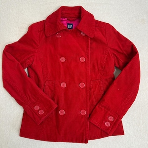 May include: A red corduroy jacket with a double-breasted design. The jacket features a notched collar, two front pockets, and red buttons. The interior lining is a bright pink color. The brand label "GAP" is visible on the inside.