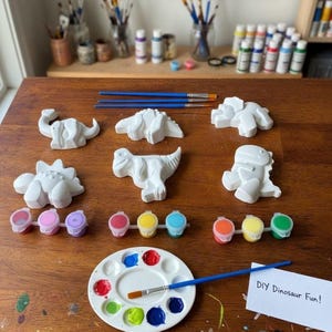 May include: A DIY dinosaur painting kit with various white dinosaur figurines, paint pots in multiple colors, paintbrushes, and a paint palette. The kit includes the text "DIY Dinosaur Fun!"