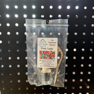May include: A car freshener diffuser in a clear plastic bag. The label reads "Fruit Loops" with a colorful cereal graphic. The net weight is .275 oz (7.8g). The product is from Cozy Home Wax Co.
