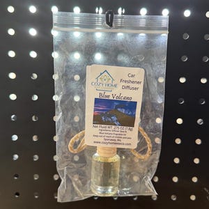 May include: A car air freshener diffuser in a clear plastic bag. The label reads "Blue Volcano" and lists the net fluid weight as .275 oz (7.8g). The bottle contains a clear liquid and is suspended by a jute string.