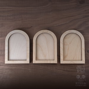 May include: Three unfinished wooden arched frames, each with a rounded top and a rectangular opening. The frames are arranged horizontally on a brown wooden surface.