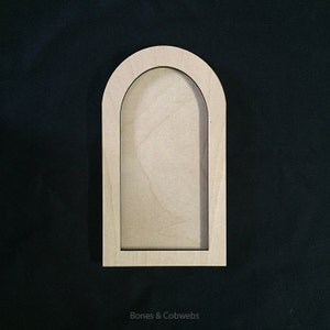 May include: A wooden arched frame with a cutout in the centre. The frame is light brown and has a natural wood finish.