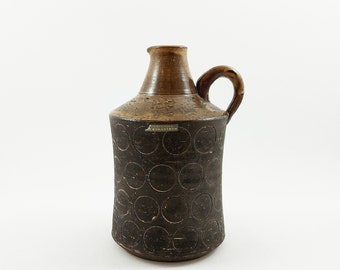 May include: A brown ceramic vase with a circular pattern and a handle. The vase is marked with the text "Stig Lindberg Bordstedt".
