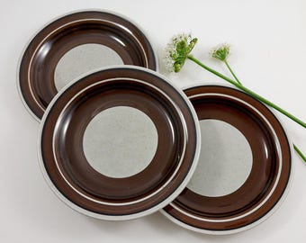 May include: Three brown and white ceramic plates with a concentric circle design. The plates have a speckled glaze and a brown rim.