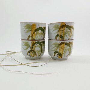 May include: Set of four white ceramic teacups with a brown rim and a yellow and green bamboo design.