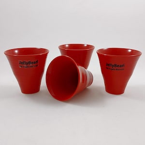 May include: Set of four red ceramic cups with a black logo that reads "JellyBean by Ingela Benson".