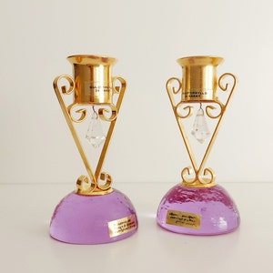 May include: Two gold candle holders with purple bases and crystal accents. The candle holders are decorated with the text "GULD-S&Oslash;LV 24 KARAT" and "FORGYLLD 24 KARAT".
