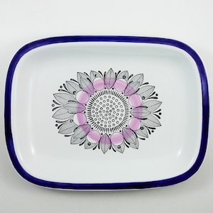 Könnte beinhalten: Eine weiße Keramik-Servierplatte mit blauem Rand und einem schwarzen und pinkfarbenen Blumendesign in der Mitte.