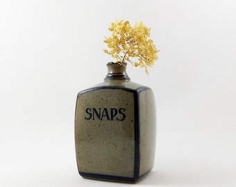 Peut inclure: Un vase en céramique avec un bord bleu foncé et le mot "SNAPS" en lettres bleues foncées. Le vase est rempli de fleurs jaunes séchées.