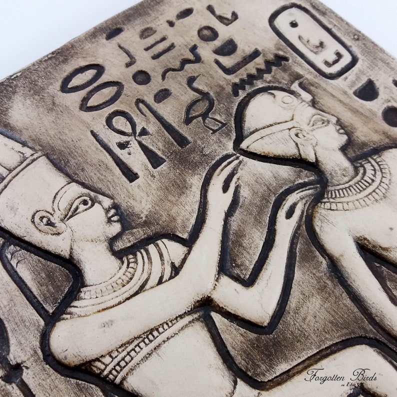 K&ouml;nnte beinhalten: Eine schwarz-wei&szlig;e Keramik-Reliefskulptur von zwei Figuren im alten &auml;gyptischen Stil. Die Figuren tragen traditionelle Kleidung und Kopfbedeckungen. Die Skulptur ist mit Hieroglyphen verziert.