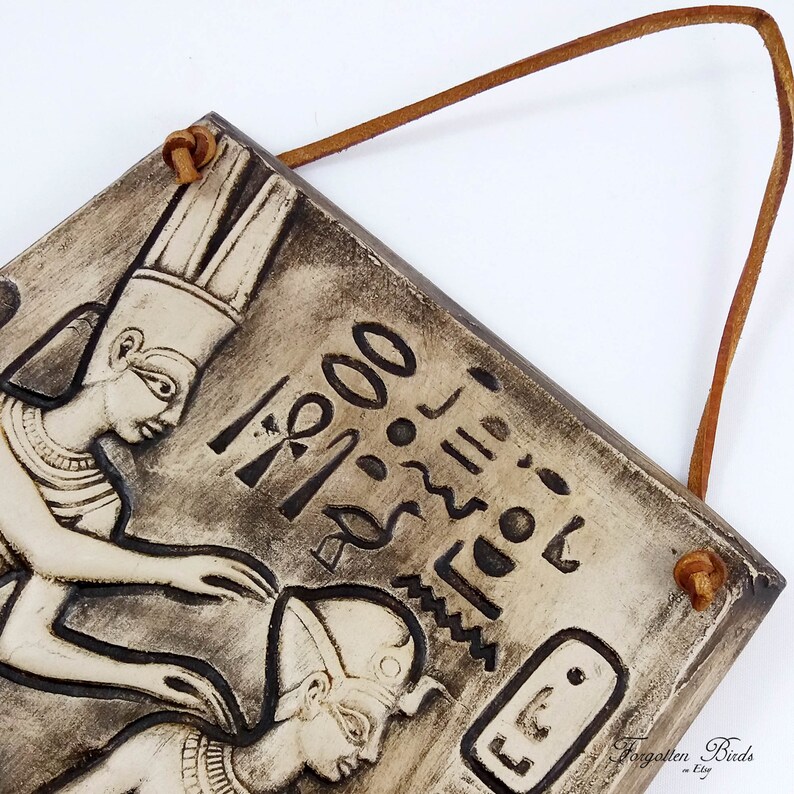 K&ouml;nnte beinhalten: Ein Keramik-Wandbild mit einer Reliefskulptur von zwei &auml;gyptischen Figuren. Die Figuren tragen traditionelle Kopfbedeckungen und Schmuck. Der Hintergrund ist mit Hieroglyphen und anderen &auml;gyptischen Symbolen verziert.