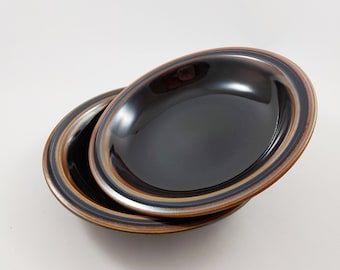 May include: Two black ceramic bowls with brown and orange stripes. The bowls are stacked on top of each other.