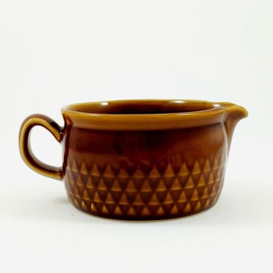 May include: A brown ceramic creamer with a geometric pattern. The creamer has a handle and a spout.