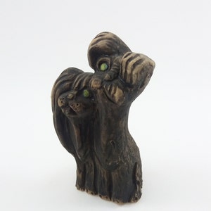 May include: A ceramic sculpture of two dogs, one standing on top of the other. The dogs are brown and have green eyes. The sculpture is a whimsical and playful depiction of two dogs.