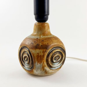 Peut inclure: Lampe de table en céramique avec glaçure marron et beige. La lampe présente trois motifs en spirale et une douille noire. La lampe a un cordon d'alimentation blanc et convient à un bureau ou une table d'appoint.