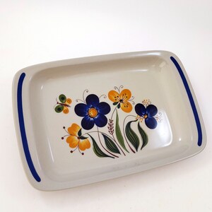 May include: Rectangular serving tray with a floral design. The tray is off-white with blue stripes on the handles. The floral design features blue and yellow flowers, green leaves, and a butterfly.