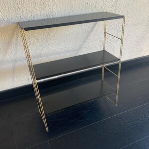 May include: A three-tiered shelf unit with a black top and shelves. The frame is gold-colored, with a twisted rope design. The shelves are rectangular and the unit is free-standing.