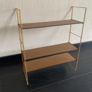May include: A gold metal shelf unit with three shelves. The shelves are made of a dark brown material.