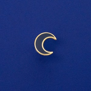 May include: A gold-coloured crescent moon pin with a dark blue enamel fill.