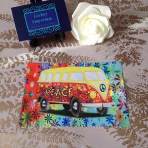 May include: A colourful microfiber cleaning cloth featuring a vintage Volkswagen bus illustration. The bus is yellow with red, blue and green accents. The words "PEACE" are printed on the side of the bus. The cloth has a floral pattern with red, orange, yellow, blue and green flowers.