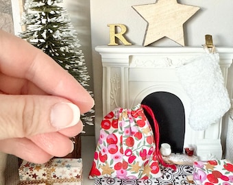 May include: Miniature Christmas scene with a white fireplace, a small Christmas tree, and wrapped gifts. A red and floral drawstring bag sits on the hearth. A wooden star and the letter "R" are on the mantel.