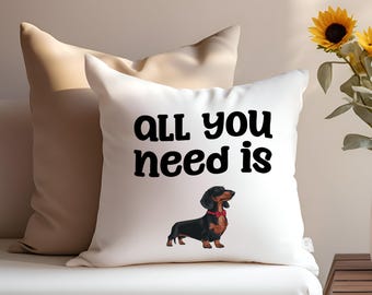 May include: White pillow with black text that reads "All you need is" and a black and brown dachshund wearing a red bow tie.