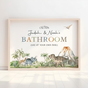 May include: A framed watercolor print featuring dinosaurs, palm trees, and a volcano. The text reads "Judah & Noah's BATHROOM (USE AT YOUR OWN RISK)" in a playful font. The artwork is set against a light background.