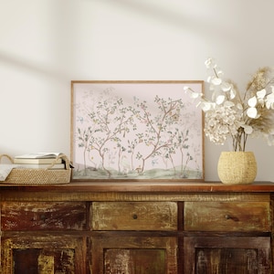 a wooden cabinet with a framed picture of trees and flowers on top of it, along with a woven basket and a vase of white flowers.