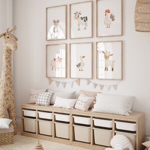 May include: A nursery room with a white wall and a wooden shelf with six storage bins. The shelf has a light brown finish and the bins are white and beige. There are six framed prints on the wall above the shelf, each featuring a different farm animal. The prints are in a watercolor style and have a light brown frame. There is a stuffed giraffe toy in the corner of the room.