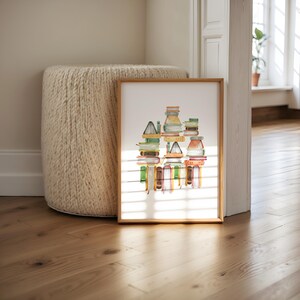 a framed artwork depicting a stack of books on a wooden floor, with a large white ottoman in the background.