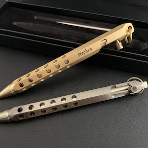 May include: Two metal pens with a hole pattern and a keyring. The top pen is gold and engraved with the name "Stephen". The bottom pen is silver.