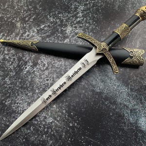 May include: A silver dagger with a black handle and gold accents. The blade is engraved with the text "Lord Stephen Matthew".