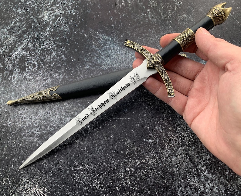 May include: A black and gold decorative dagger with a silver blade. The blade is engraved with the text "Lord Stephen Matthew".