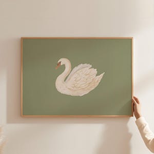 May include: A framed print featuring a white swan with a peach-colored beak and a detailed wing design. The swan is set against a muted green background. The frame is made of light-colored wood.